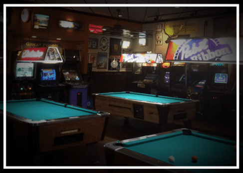 A room with several pool tables and video games.